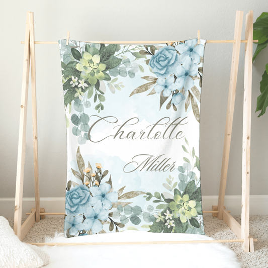 Personalized minky plush blanket hanging on a wooden hanger featuring beautiful serene watercolor blue and green floral design.